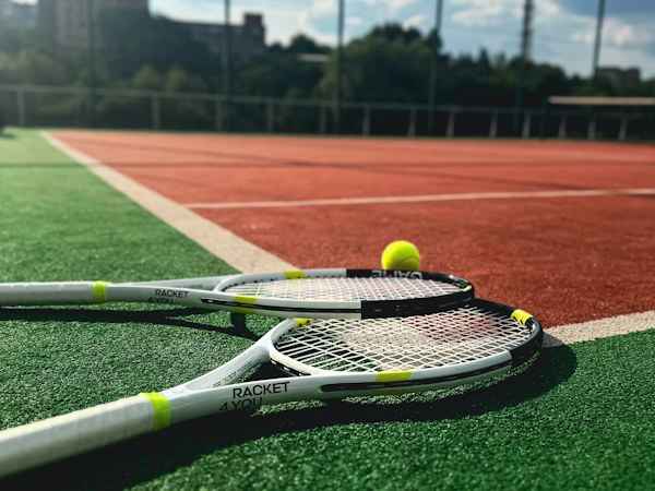 Tennisschläger und gelber Ball auf einem roten und grünen Platz